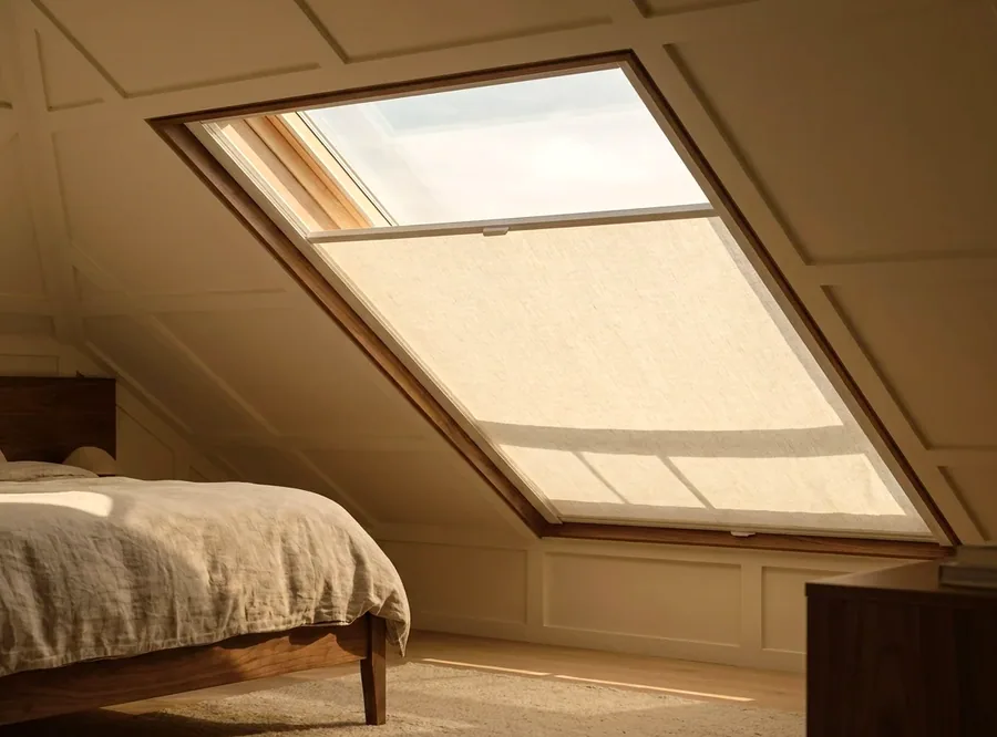 A tensioned blind fitted to a raked skylight in an attic bedroom, holding flat against the glass